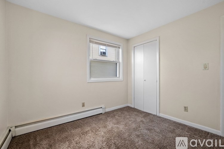 A room with a carpeted floor, a window with blinds, and a door.