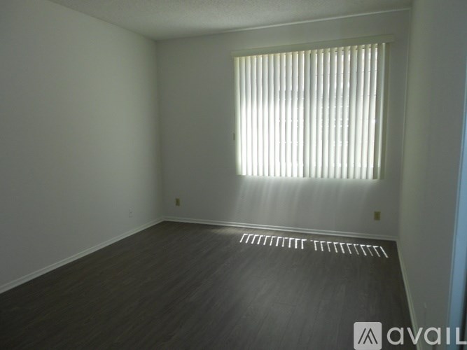 A room with a window covered by white blinds and wooden flooring.