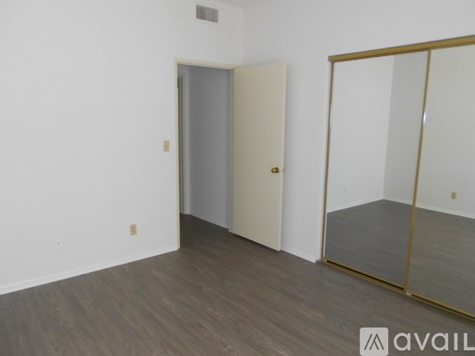 A room with a white wall and a wooden floor with a mirror on the right side.