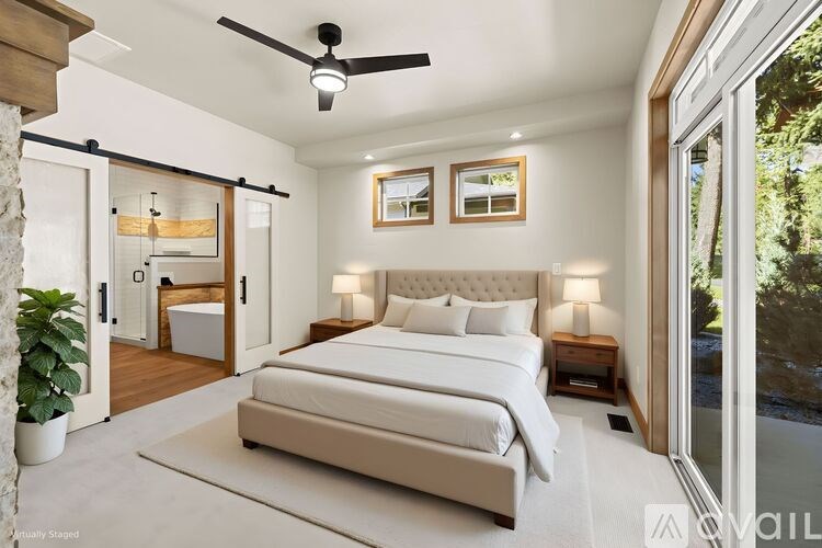 A bedroom with a large bed, a ceiling fan, and a view of the outdoors through a sliding glass door.