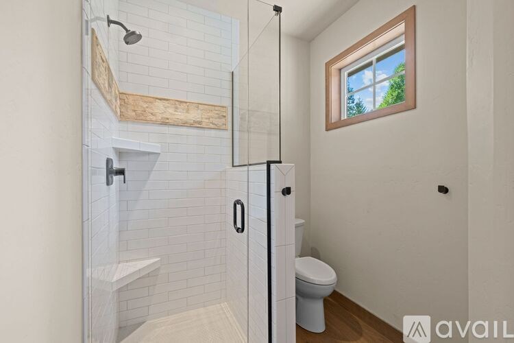 A white tiled bathroom with a window and a toilet.