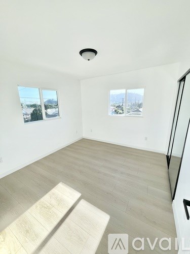 A spacious room with wooden flooring and two windows.
