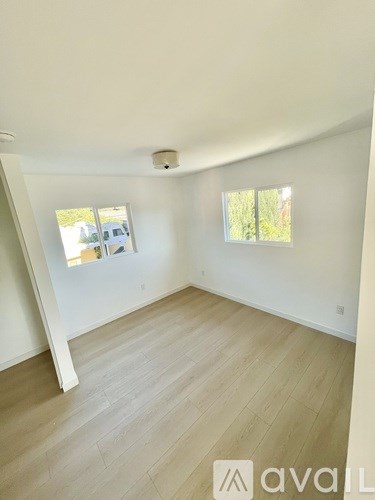A room with wooden flooring and two windows.