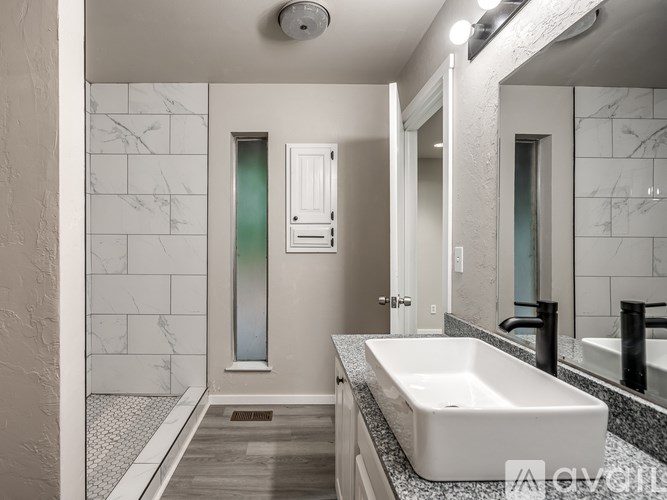 A modern bathroom with a white sink and a glass shower door.