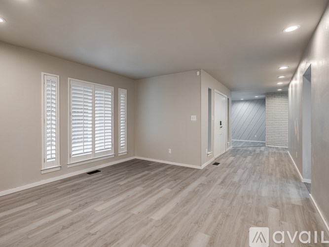 A spacious room with wooden flooring and white shutters on the windows.