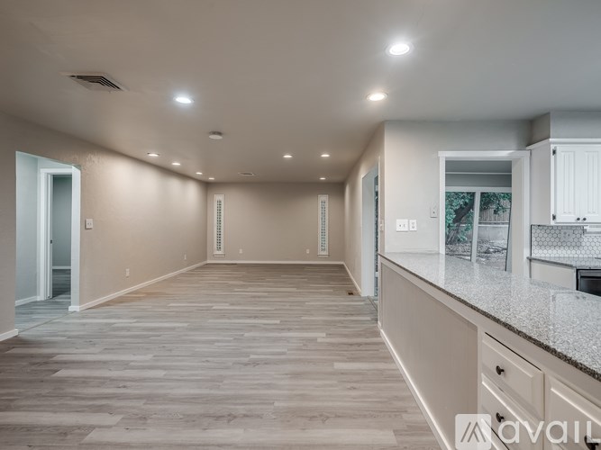A spacious room with wooden flooring and a kitchen area with white cabinets.