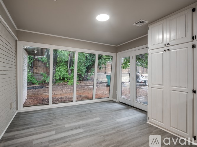 A room with white walls and a wooden floor with a sliding glass door leading to a backyard.