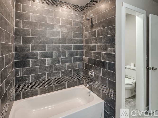 A bathroom with a white tub and grey tiled walls.