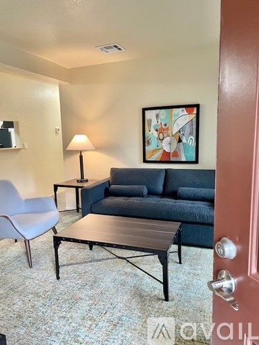 A living room with a blue couch, a white chair, and a painting on the wall.