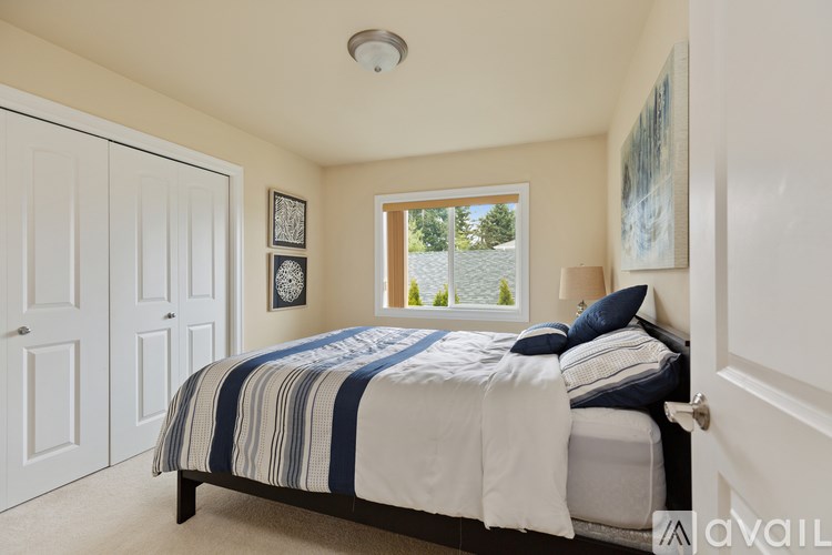 A bedroom with a bed, a window, and a painting on the wall.