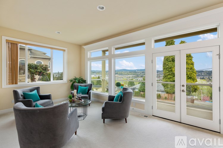 A living room with a grey couch, a glass table, and a view of the outdoors through the windows.