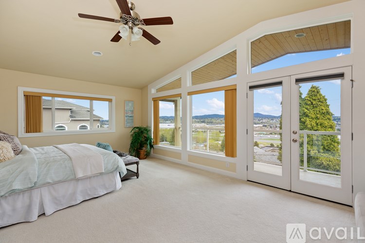 A bedroom with a bed, a ceiling fan, and a view of the outdoors through the windows.