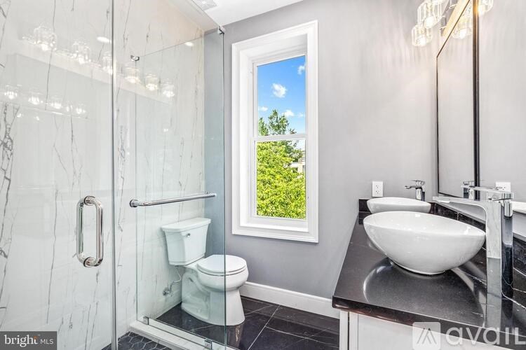 A bathroom with a toilet, sink, and a window showing a green landscape.