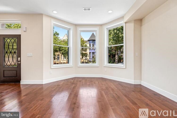 A spacious room with wooden floors and a view of a building through the windows.
