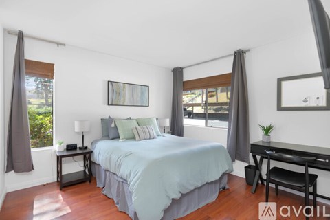 A bedroom with a bed, desk, and window with curtains.