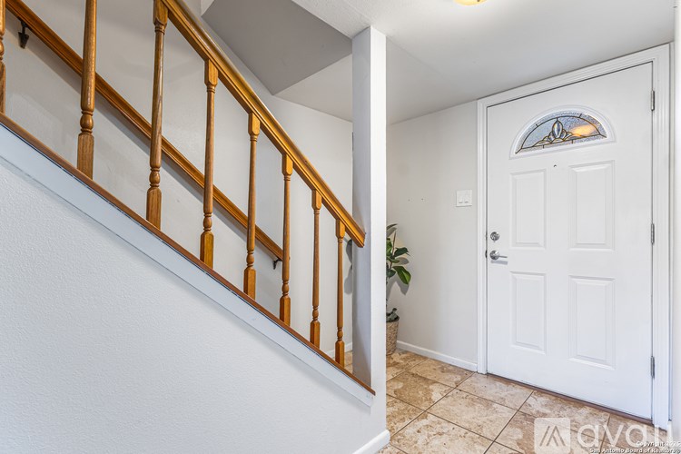 A white door with a stained glass window is in a room with a white wall and a wooden staircase.
