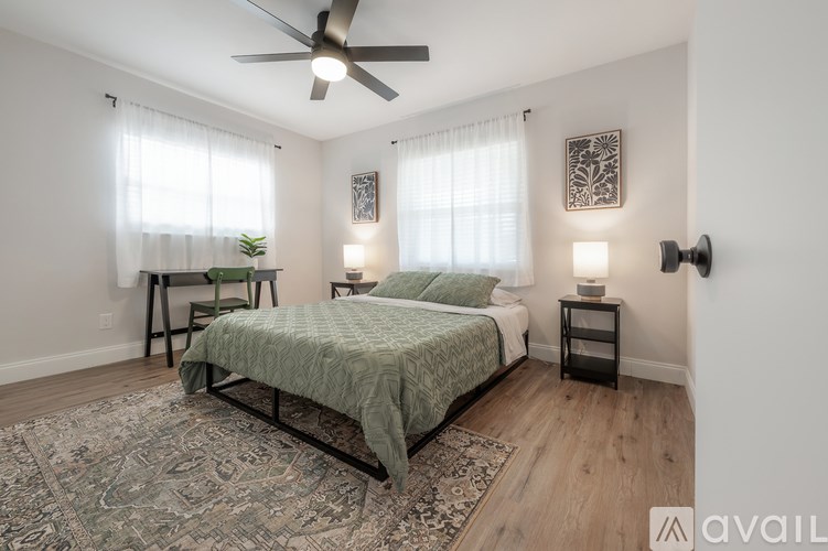 A bedroom with a bed, a chair, a ceiling fan, and two wall lamps.