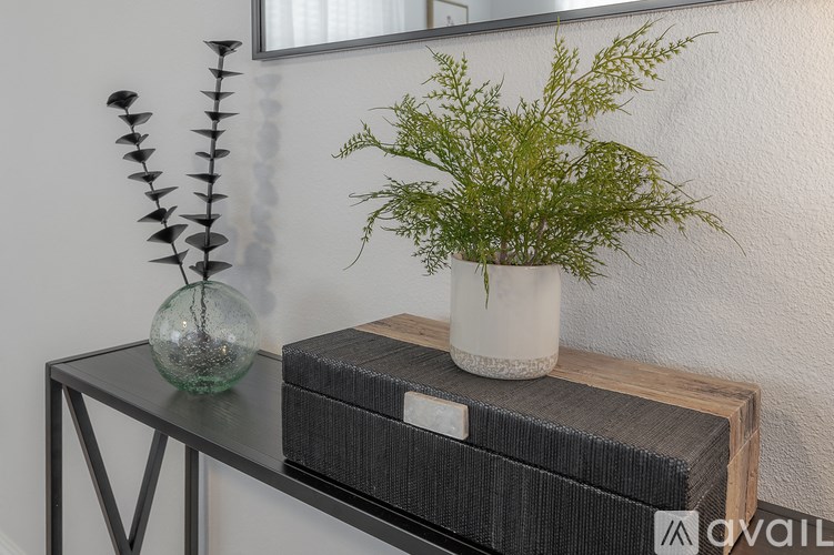 A glass vase with a plant in it sits on a wooden table.