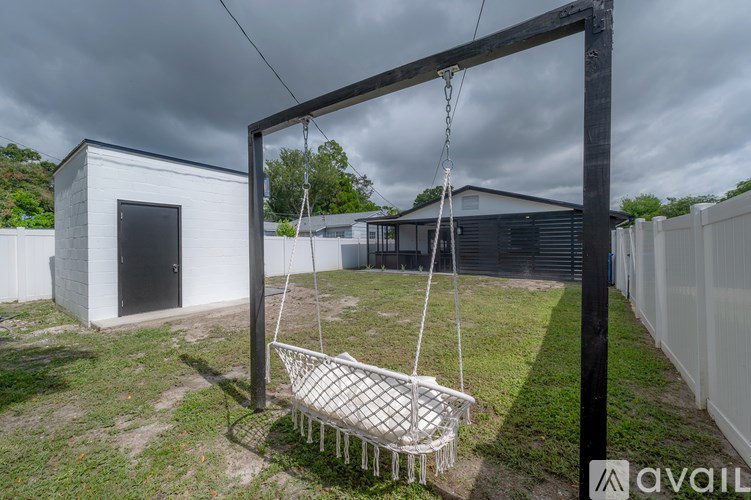 A white swing hangs from a wooden frame in a backyard.