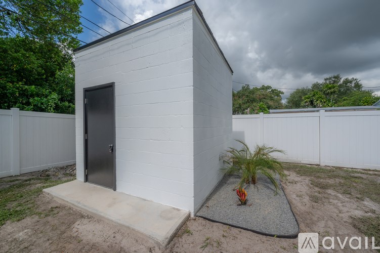 A small white building with a door and a window is surrounded by a white fence.