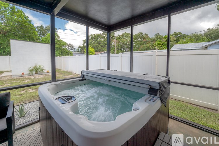 A hot tub is on a patio with a view of a white fence and trees.