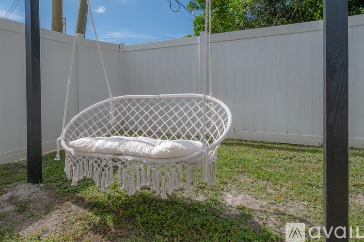 A white hanging bed with a white mattress is suspended by ropes in a backyard.