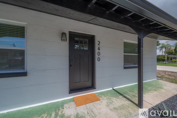 A house numbered 2400 with a black door and a brown mat on the concrete.