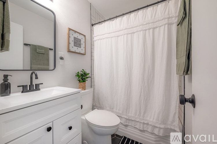 A white bathroom with a toilet, sink, mirror, and shower curtain.