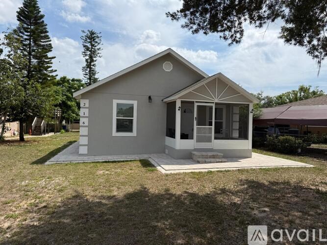 A small house with a porch is surrounded by trees and grass.