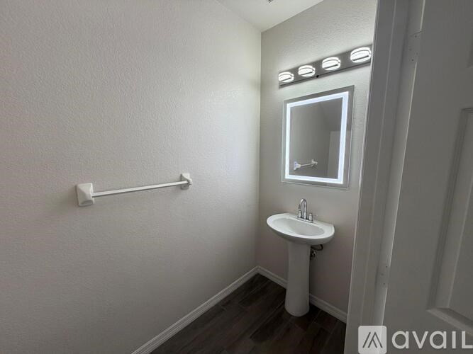 A white sink is in a white bathroom with a mirror and lights above it.