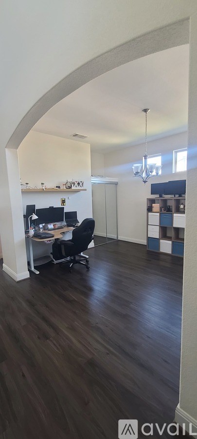 A room with a wooden floor and a white wall with a black chair and a desk.