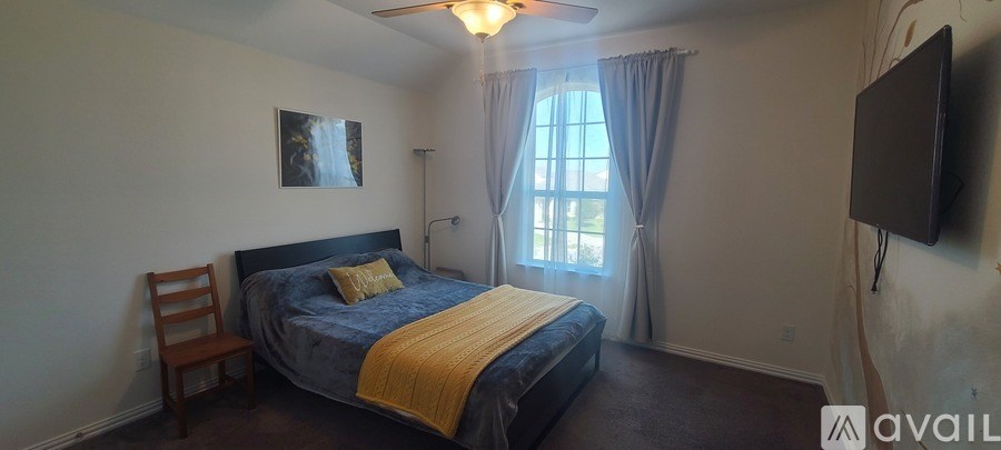 A bedroom with a bed, chair, window, and a flat screen TV mounted on the wall.