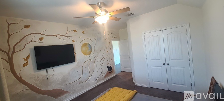 A room with a tree mural on the wall and a ceiling fan.