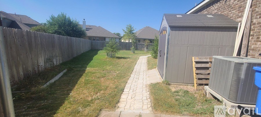 A backyard with a wooden fence and a concrete pathway.