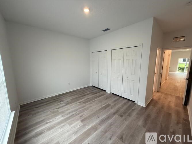 A room with a wooden floor and white walls, with two white doors and a window on the left.