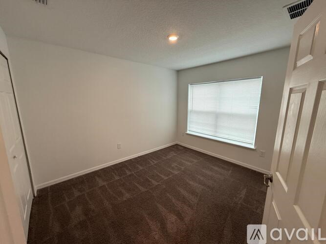 A room with a carpeted floor and a window with blinds.