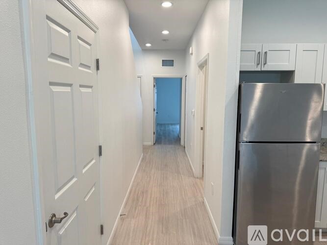 A kitchen with a refrigerator on the right and a door at the end of the hallway.