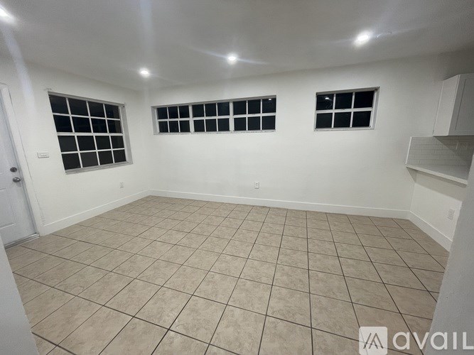 A room with beige tiled flooring and white walls, with two windows and a door.