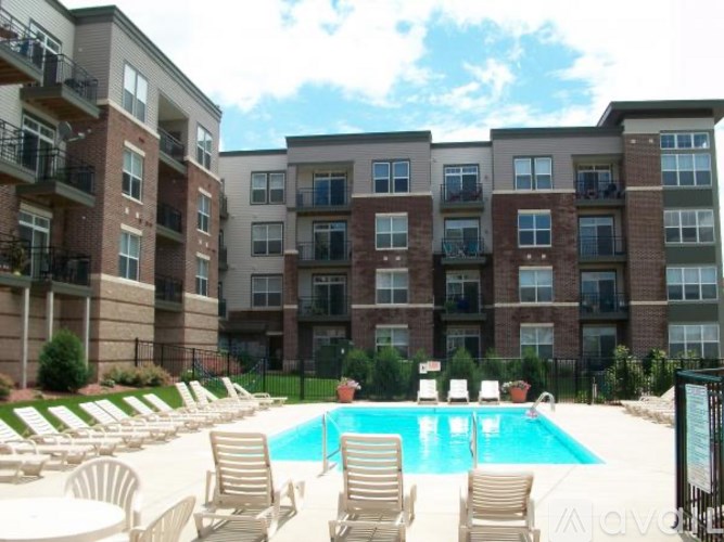 A pool surrounded by lounge chairs in front of apartment buildings.