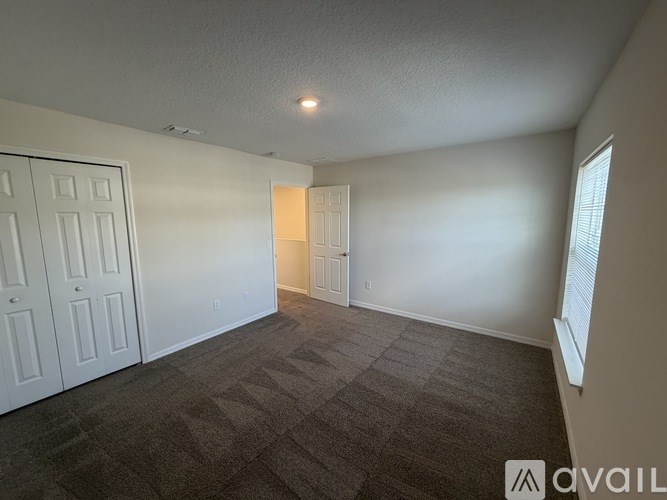 A room with carpeted floor, two doors, and a window with blinds.