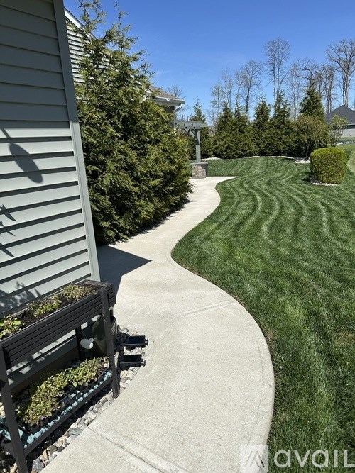A bench sits on a concrete walkway next to a green lawn.