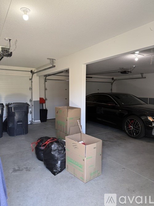 A black car is parked in a garage with boxes and bags on the floor.