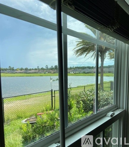 A view from a window looking out to a body of water with a fence and greenery.
