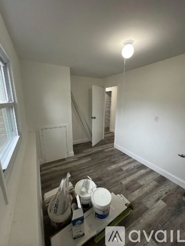 A room with a white ceiling and wooden floor with paint buckets and a paint roller.