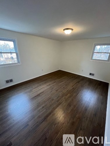 A room with wooden flooring and two windows.