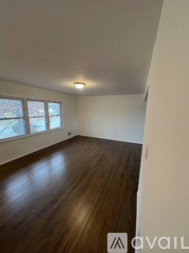 A room with wooden flooring and a window showing a view of trees outside.