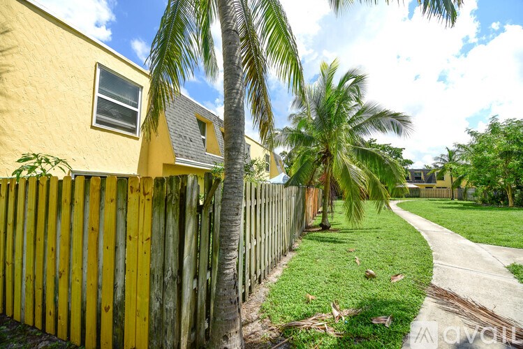 A yellow house with a wooden fence and palm trees in the background.