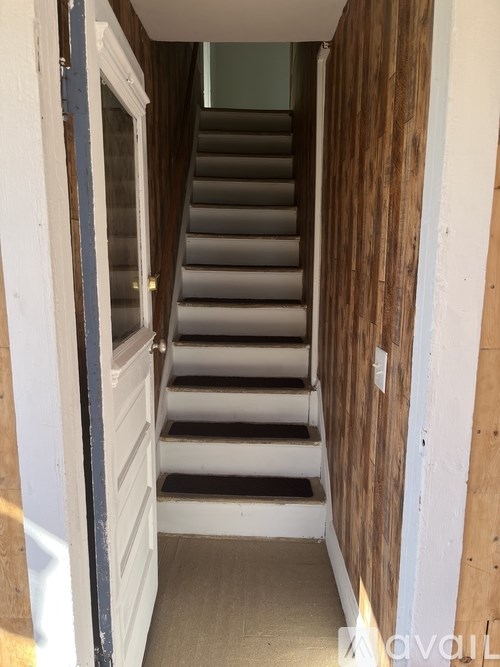 A staircase with a white door on the left and a wooden wall on the right.