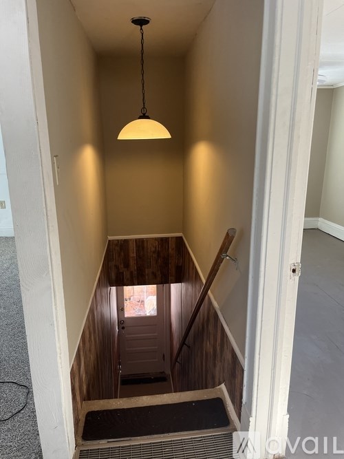 A hallway with a wooden staircase and a hanging light fixture.