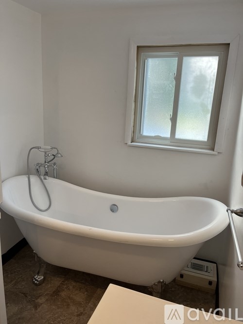 A white bathtub with a shower head and a window above it.